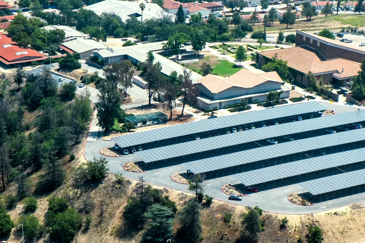 Vista aérea de um conjunto com vários prédios distintos dividindo o mesmo terreno e estacionamento coberto por painéis solares